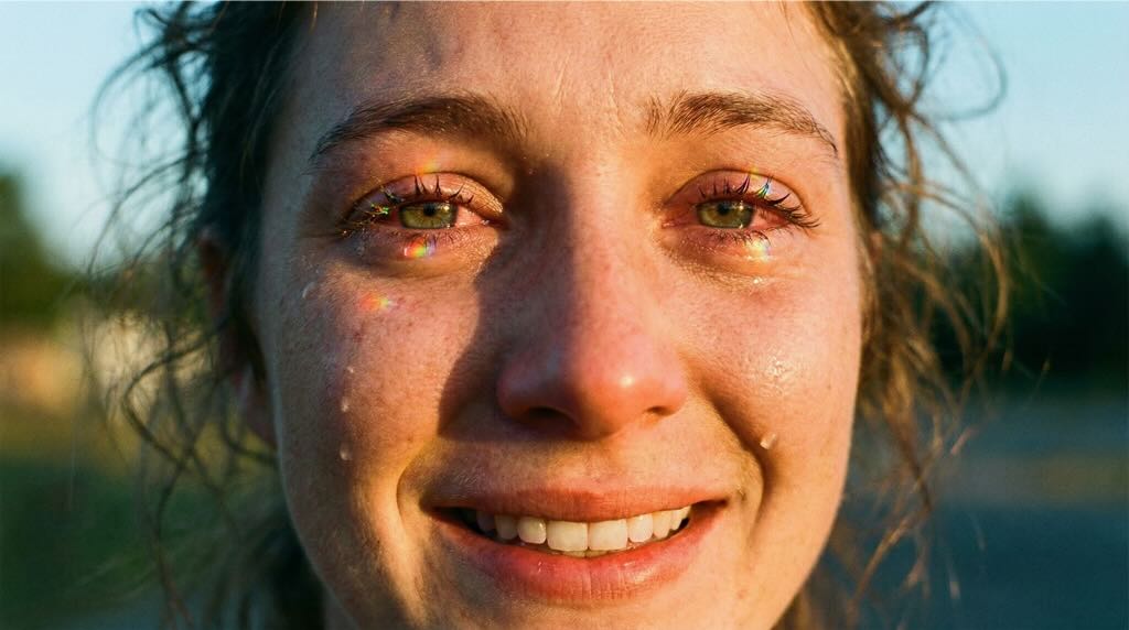 Close-up de rosto chorando e sorrindo sob luz solar vibrante, representando a complexidade emocional e o sacrifício do tipo de amor Agape.